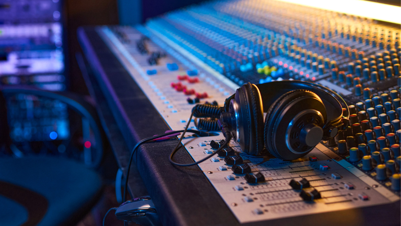 Headphones beside music records and a laptop displaying music data analysis
